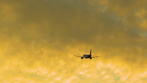 airplane during flight flying against bright orange sky at dusk