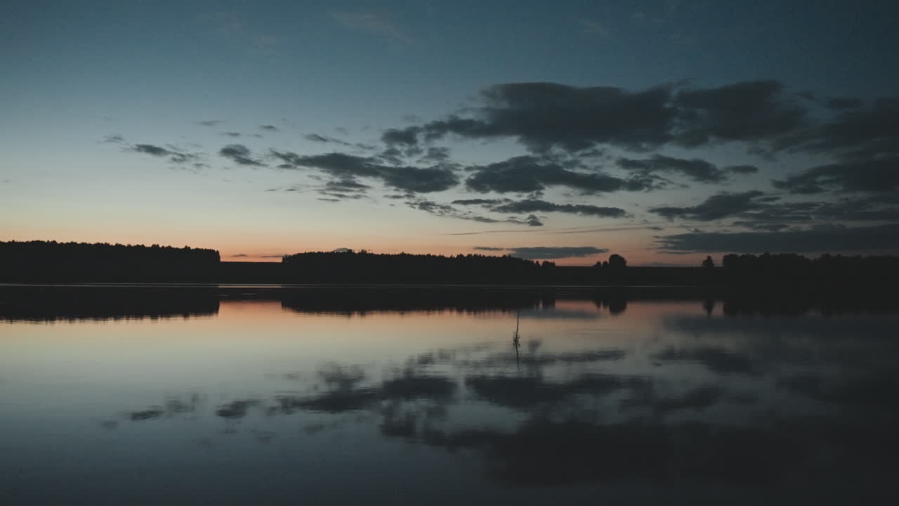 Lakeside dusk reflection calm water, horizon line and cloud silhouettes mirrored on still surface, subtle orange glow on skyline, quiet camping atmosphere and tranquil nature retreat perfect