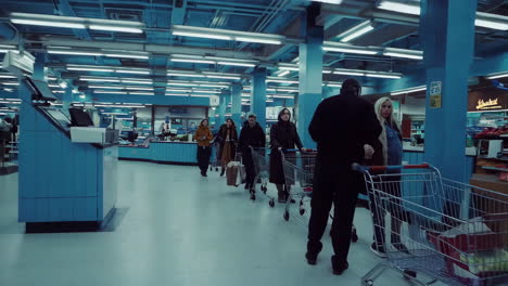 people shopping and waiting in a dimly lit, blue-toned supermarket