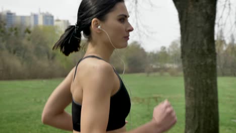 young motivated girl is jogging in park in summer, listening to music, healthy lifestyle, sport conception, side view