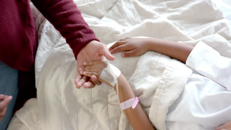 holding hands of african american mother and daughter lying in hospital bed, slow motion