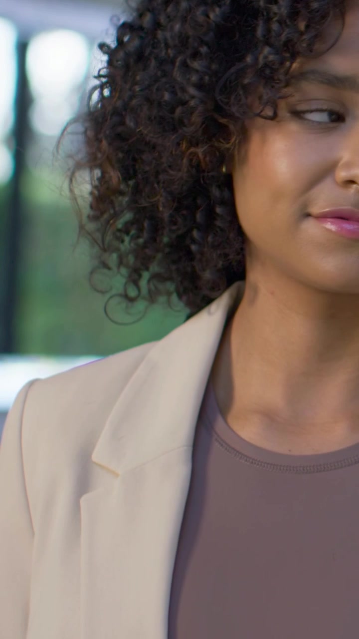 Vídeo vertical: Câmera recuando revelando mulher de blazer bege lendo na janela, planta, espaço para texto