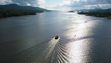A-4K-rising-following-aerial-shot-of-a-tourist-boat-sailing-towards-the-open-sea-in-the-sunshine-in-Kenmare-Bay