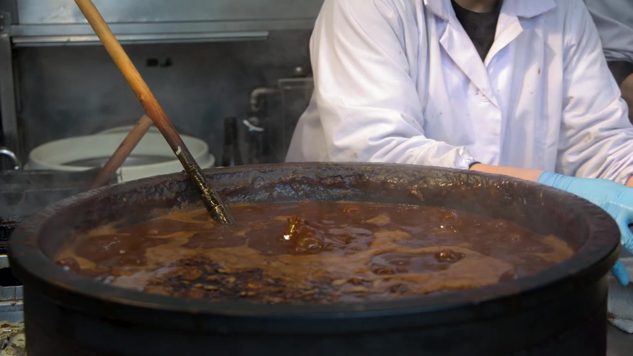 A chef in white uniform stirs a large steaming pot of miso stew in Tokyo