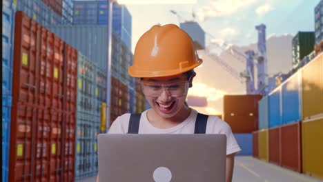 primer plano de una trabajadora asiática con gafas de protección y casco de seguridad mirando la computadora portátil y luego gritando gol celebrando mientras estaba de pie en el almacén del patio de contenedores