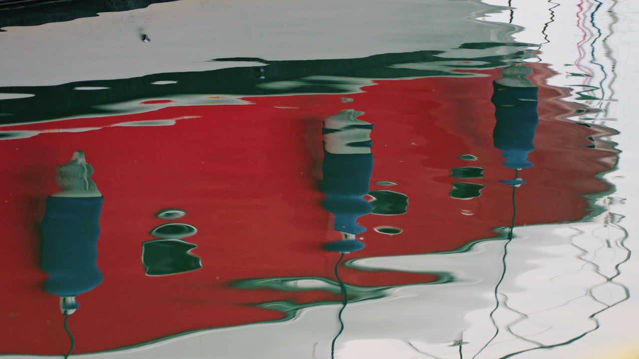Modern red and white yacht docked in calm marina waters with clear reflections