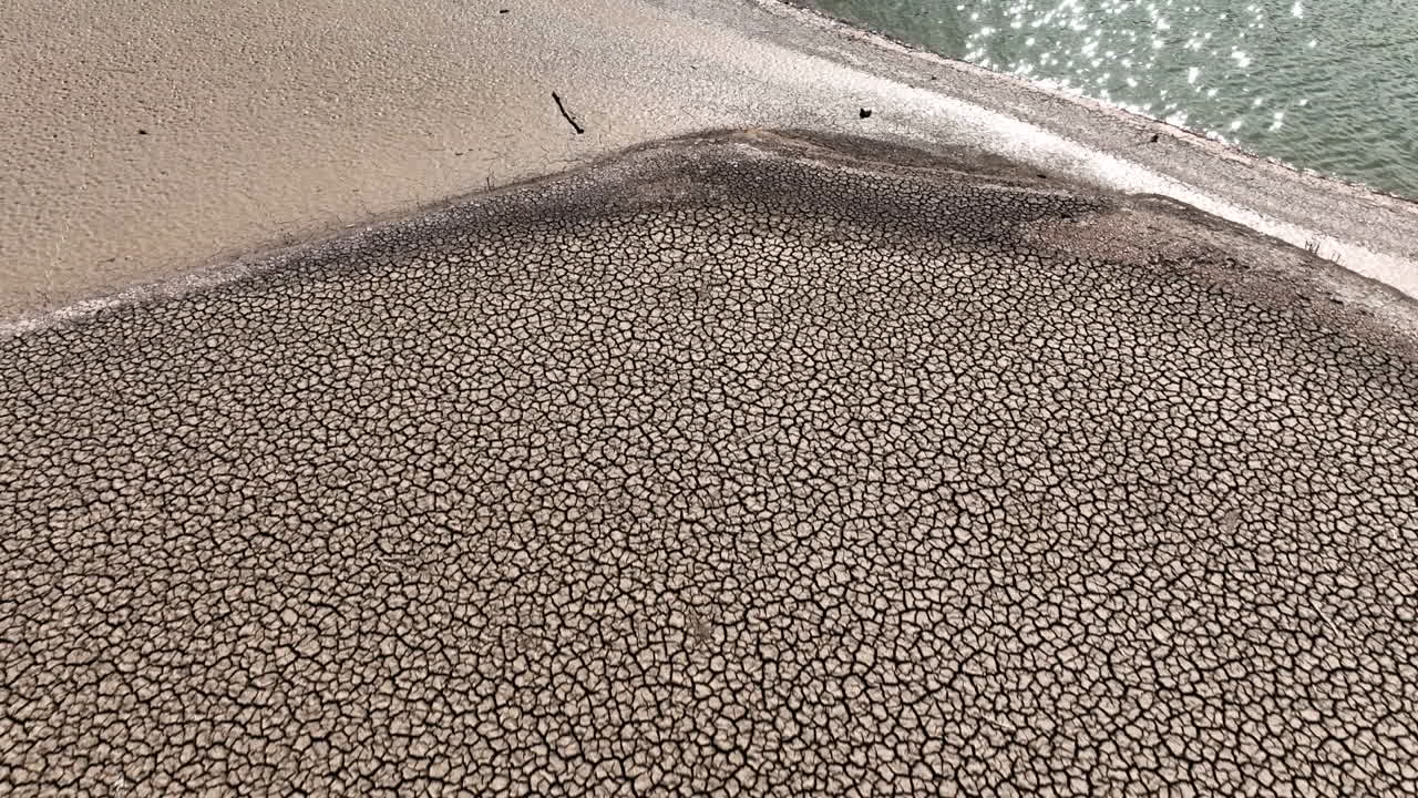 대조적인 공중 전망은 건조한 균열 된 가 ⁇  땅을 내려다보고 반 ⁇ 이는  ⁇ 빛 반 ⁇ 이는 강 물을 가로질러 이동