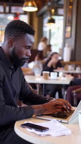 determined afro businessman working on laptop in coffee bar