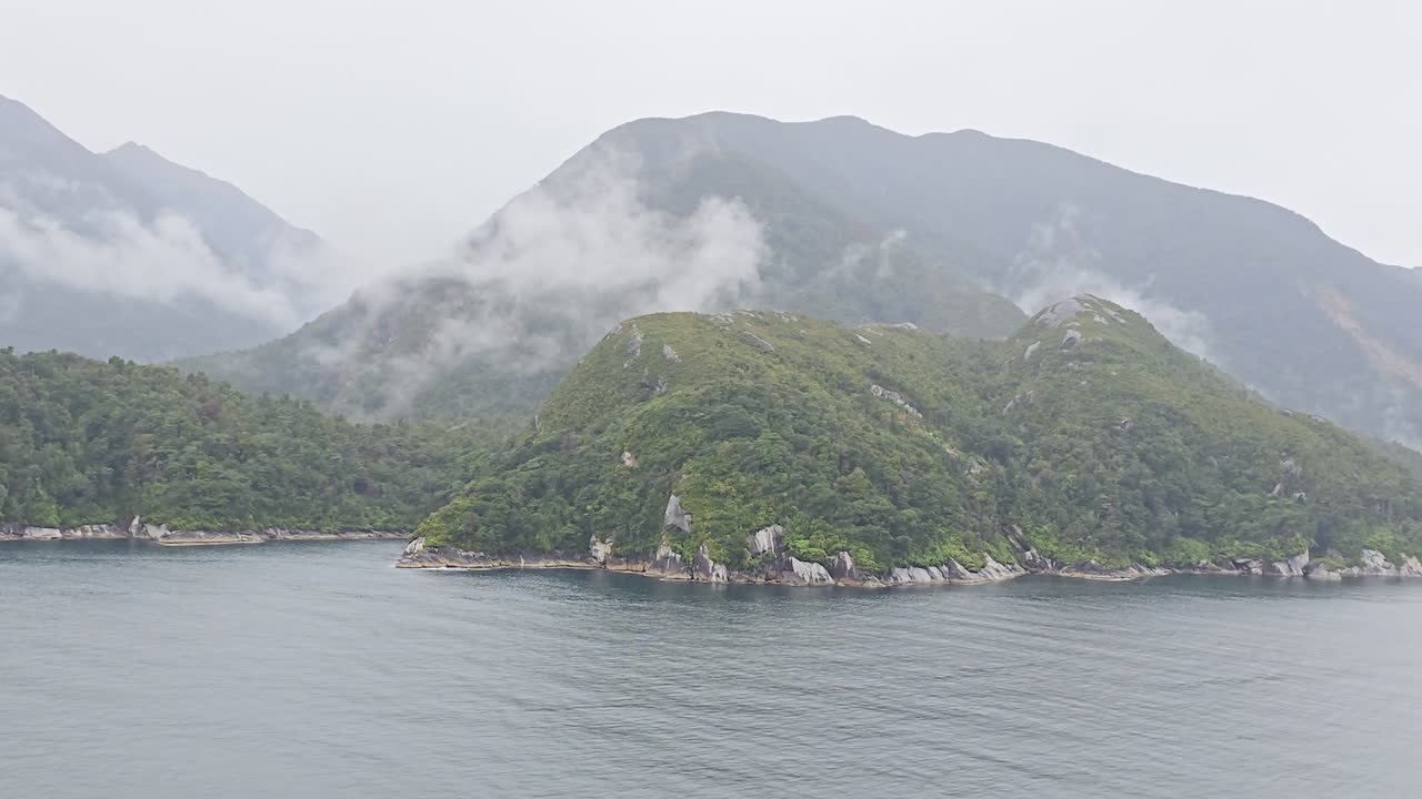 Milford Sound fiord presenting moody natural landscape with steep, forested mountains emerging through misty clouds, reflecting the dramatic and untouched wilderness of New Zealand