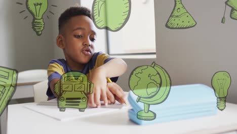 Animation-Grüner-Schulsymbole-über-Einem-Glücklichen-Afroamerikanischen-Schuljungen,-Der-Im-Unterricht-Am-Schreibtisch-Arbeitet