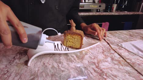 latin male barista waiter decorating a chocolate cake in a white plate with chocolate sauce at a cafeteria coffee shop restaurant in mexico latin-america