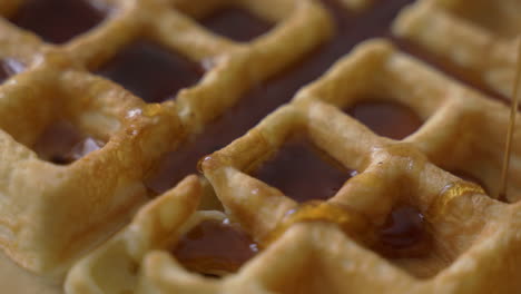 girando hacia arriba una vista macro cercana de waffles dorados y crujientes siendo rociados con jarabe de arce dulce