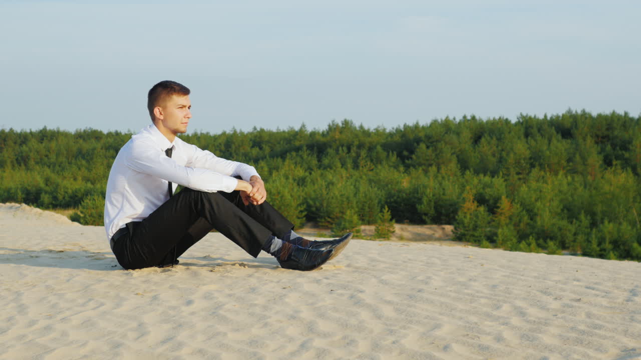 양복을 입은 젊은 사업가가 모래 위에 앉아 있다