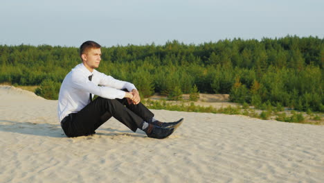 a young businessman in a suit sits on the sand