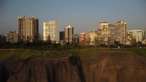 AERIAL---Cliffs,-coastline-in-luxurious-Miraflores,-Lima,-Peru,-wide-rising-shot