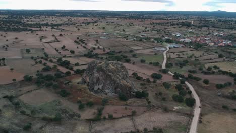 Aerial-orbit-shot-of-a-gigantic-rock-on-flat-terrain-near-a-small-town