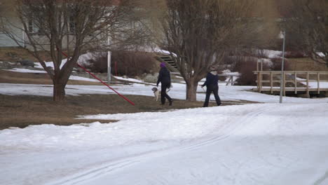 Dog-playing-and-people-walking-in-the-snow-with-sticks-in-Vuokatti-Finland,-handheld,-Movement