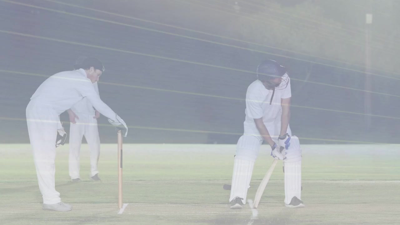 Wicketkeeper klapper og gestikulerer, slagmand banker og justerer benskinner, forbereder sig på bolden under lys.