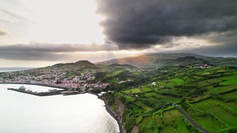 aufsteigende drohnenaufnahme der insel faial auf den azoren bei sonnenuntergang mit grüner vegetation und der stadt horta im hintergrund