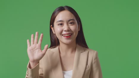 close up of asian business woman waving hand and smiling while standing on green screen in the studio