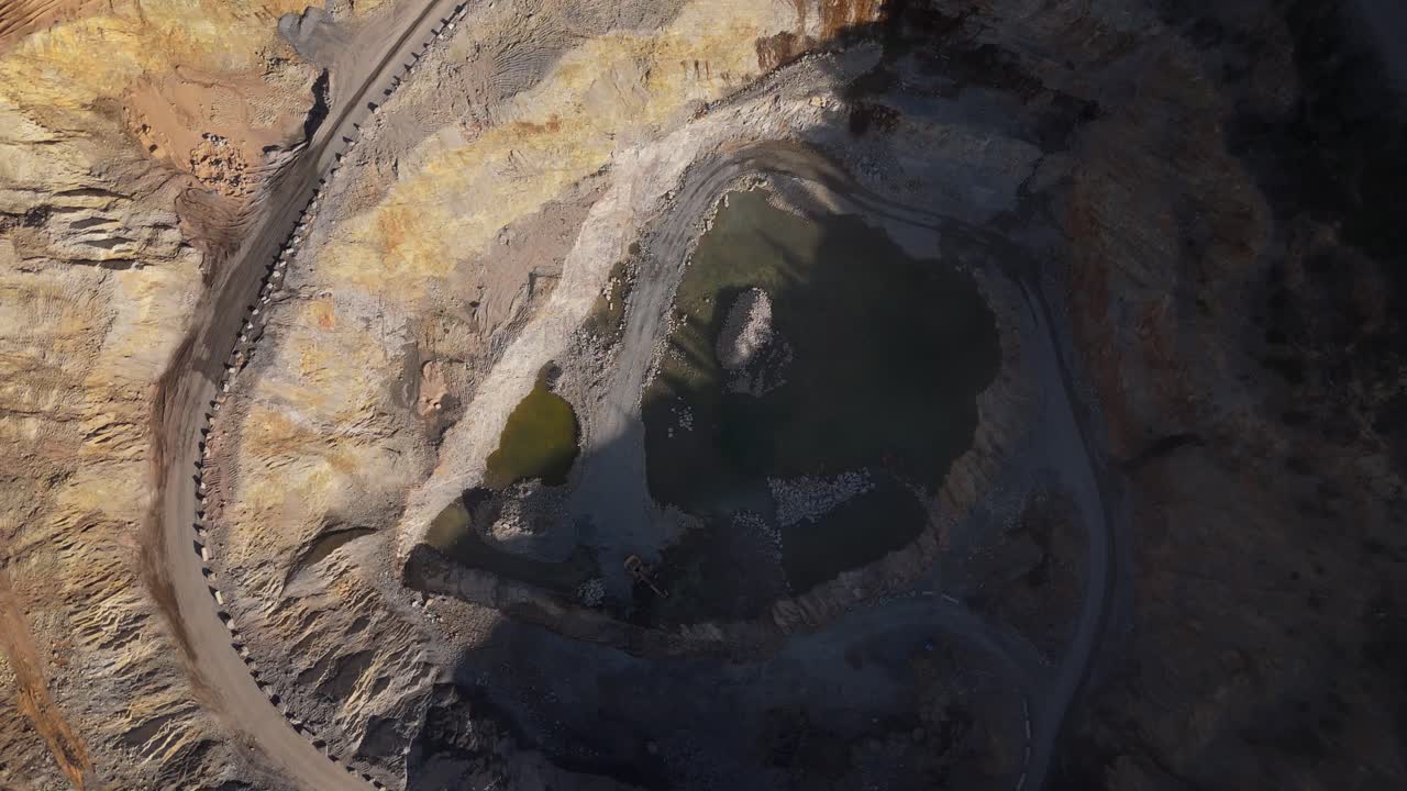 Aerial drone view of an active mine with conveyor belts moving crushed rock towards quarry stockpiles under bright sunlight