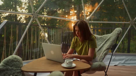 busy woman freelancer uses laptop to work online at home sitting in armchair with cup of coffee in morning. focused woman corrects hair falling on face