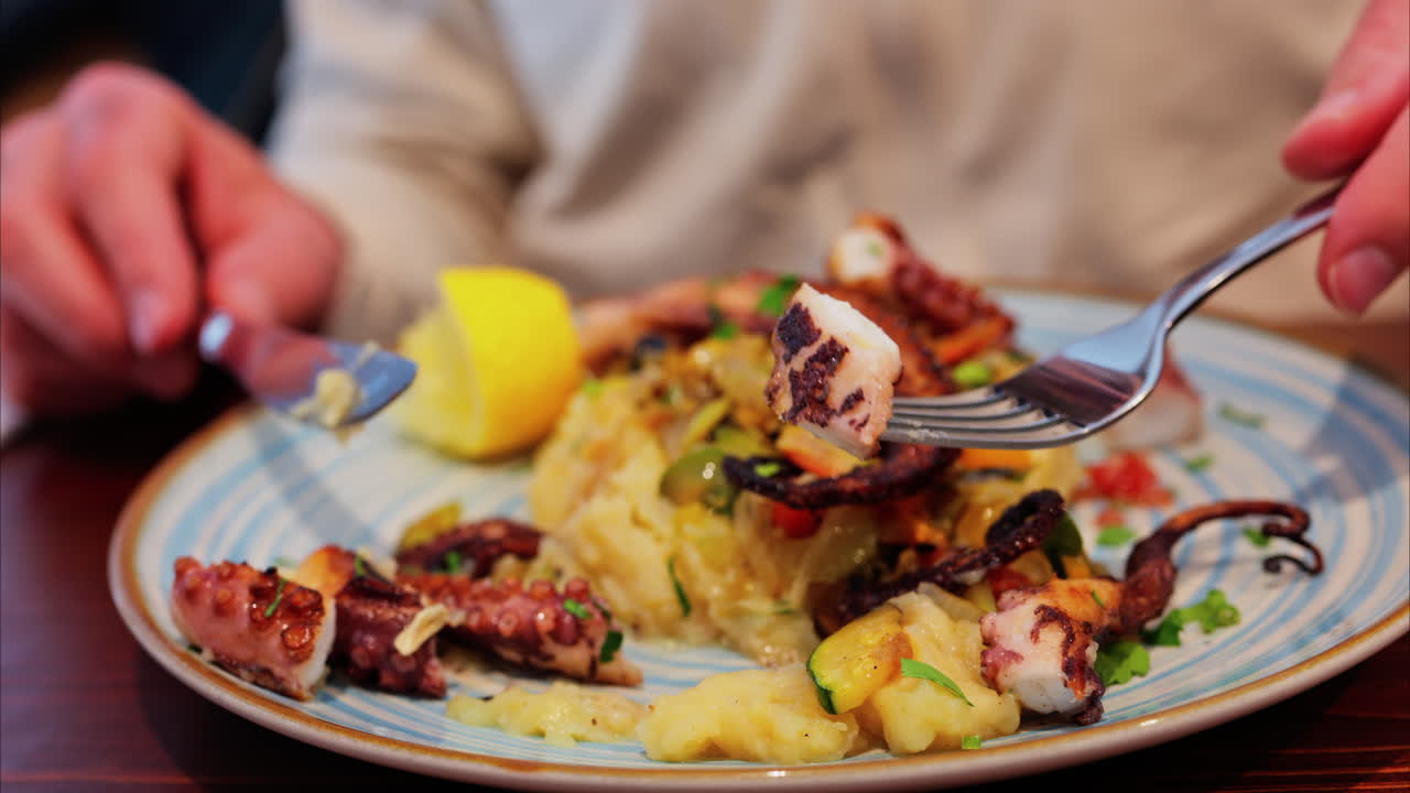 Close up of a man cutting and eating grilled octopus on a puree at a restaurant