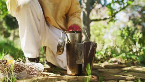 Caucasian-male-beekeeper-in-protective-clothing-preparing-smoker