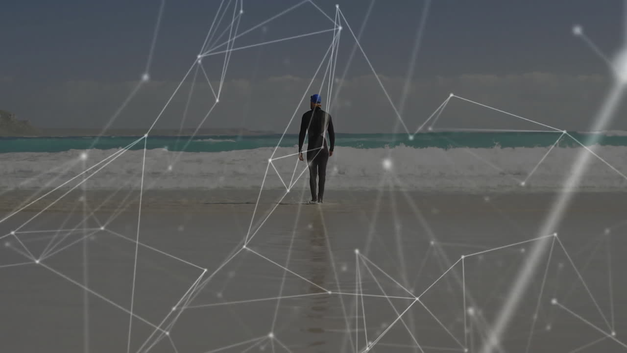 Person in wetsuit walking on beach with network connections animation overlay