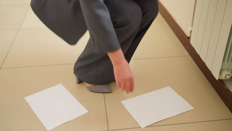 closeup of businesswoman wearing grey trousers and heels standing on tiled office floor with blank white paper sheets scattered around feet suggesting dropped documents