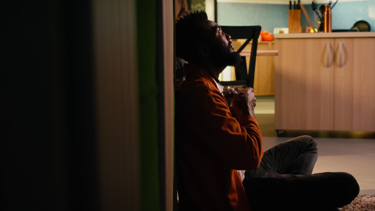 Depressed black man sitting on the floor in a dark hallway