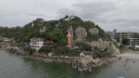 Drone-Volando-Hacia-La-Estatua-Dorada-De-Buddha-En-Las-Rocas-En-El-Mar