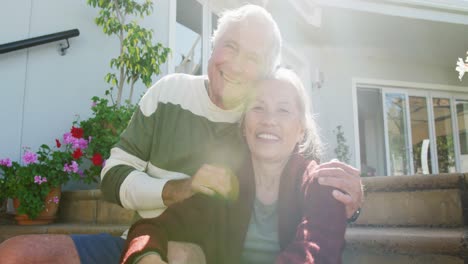 portrait of happy diverse senior couple sitting on stairs on sunny day in garden