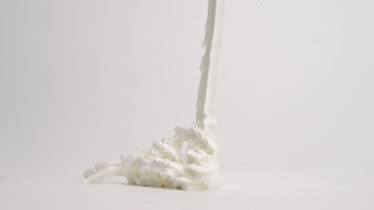 ленты белых взбитых сливок падают в кучу на белой столешнице и поливаются насыщенным коричневым шоколадным сиропом для идеального мороженого в замедленной съемке