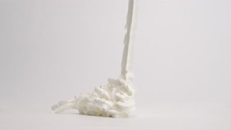 cintas de crema batida blanca que caen en una pila sobre la mesa blanca y se rocían con un rico jarabe de chocolate marrón para un helado perfecto en cámara lenta