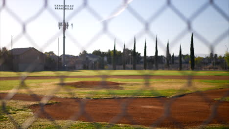 Deslice-Hacia-Arriba-La-Toma-Mirando-Un-Diamante-De-Campo-De-Béisbol-Verde-Vacío-Desde-Detrás-Del-Plato-De-Home-Y-Una-Cerca-De-Eslabones-De-Cadena-En-Un-Parque-Público-Temprano-En-La-Mañana