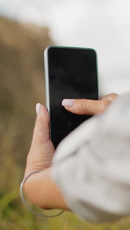 vista de cerca de la mano de la dama de manga larga tomando una foto de alguien con la pierna colocada en el heno estacionado, el fondo está ligeramente borroso, destacando el enfoque en la fotografía de teléfonos inteligentes en un paisaje rural