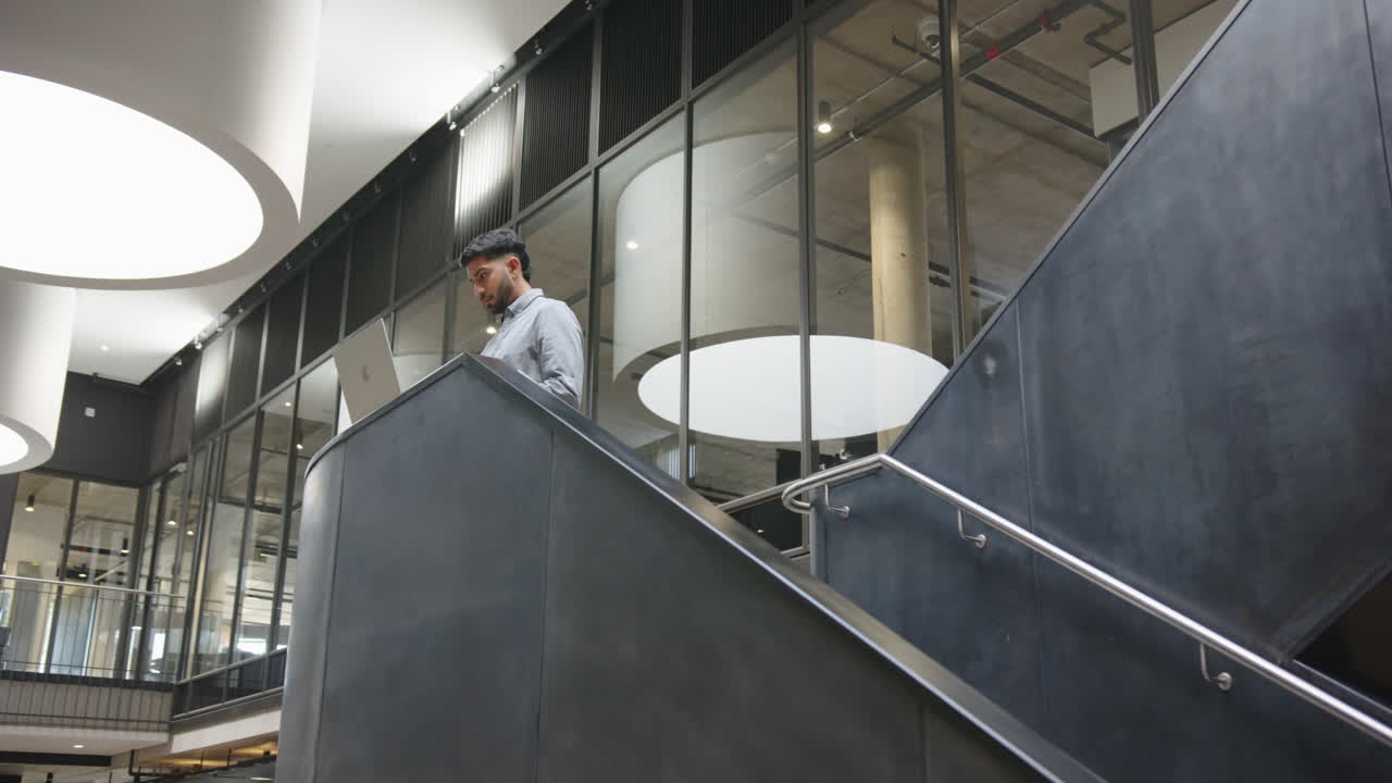 Walking down stairs, businessman holding laptop in modern office building