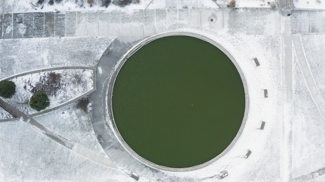 공원에서 녹색 물의 원형 연못을 직선 아래로 보는 눈이 많은 날 공중 - 겨울 타이틀을위한 훌륭한 배경