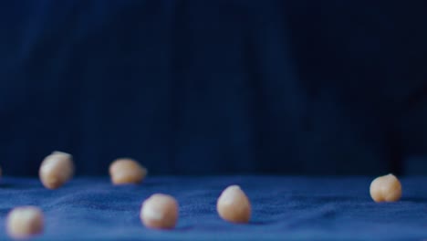 Chickpeas-fall-in-slow-motion-rain,-in-the-background-and-as-a-base-there-is-an-electric-blue-fabric