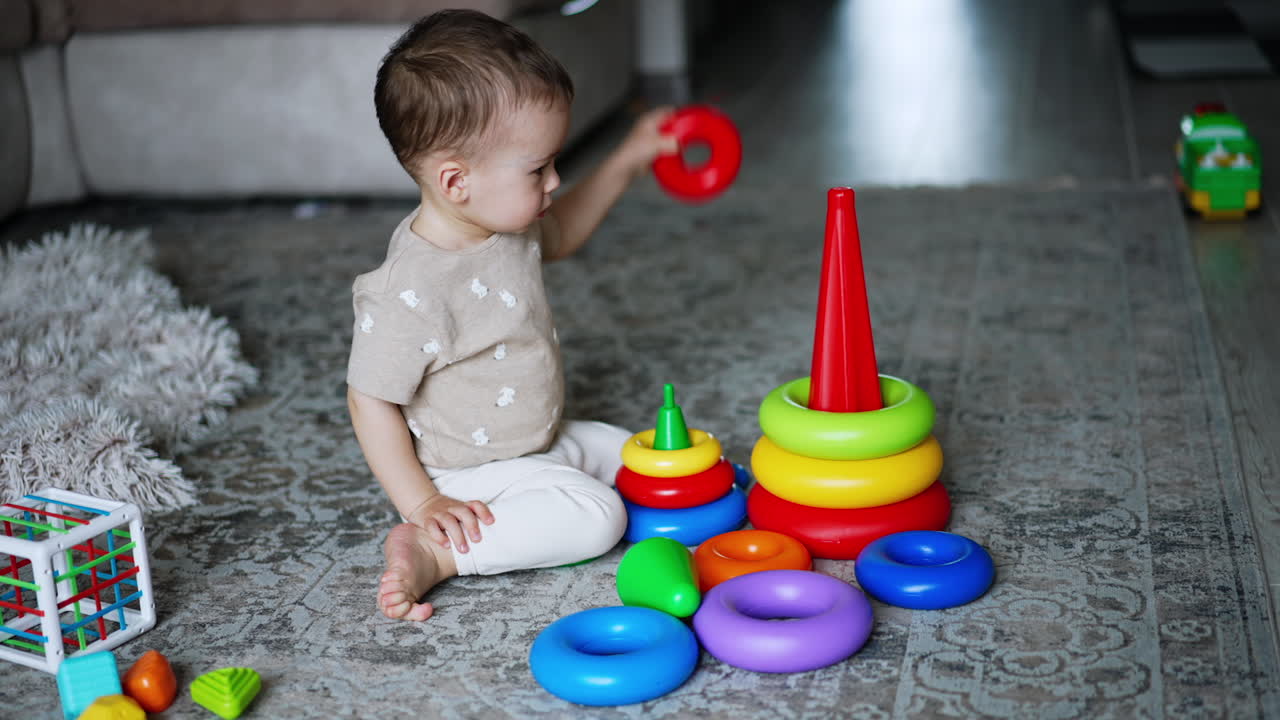 One year old toddler disassembling the toy pyramids. Little baby boy plays on the floor at home. High angle view.