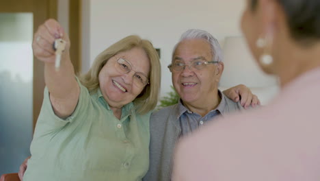 feliz pareja mayor mirando la cámara y mostrando las llaves de su nueva casa