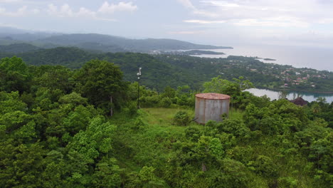 Vista-Aérea-Que-Se-Eleva-Sobre-La-Cima-De-Una-Ladera-De-Los-Drapers-Para-Revelar-Port-Antonio-En-La-Distancia-Con-La-Isla-Marina-Mientras-La-Cámara-Continúa-Descendiendo-Hacia-El-Valle-De-Abajo