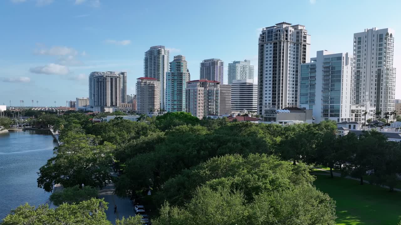 Aerial zoom shot of river, green trees in park in front of skyline downtown of Saint Petersburg, Florida. Sunny day with blue sky. Residential apartment Towers with Beautiful view, USA.