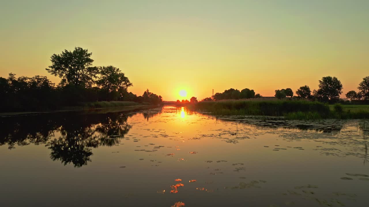 일출 시 반사되는 잔잔한 호수 위로 날아가는 멋진 드론 공중 샷