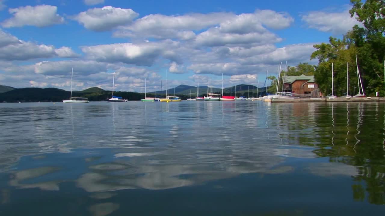 흐린 푸른 하늘과 범선이 버몬트 중부의 유리 같은 시골 호수 멀리서 보입니다.