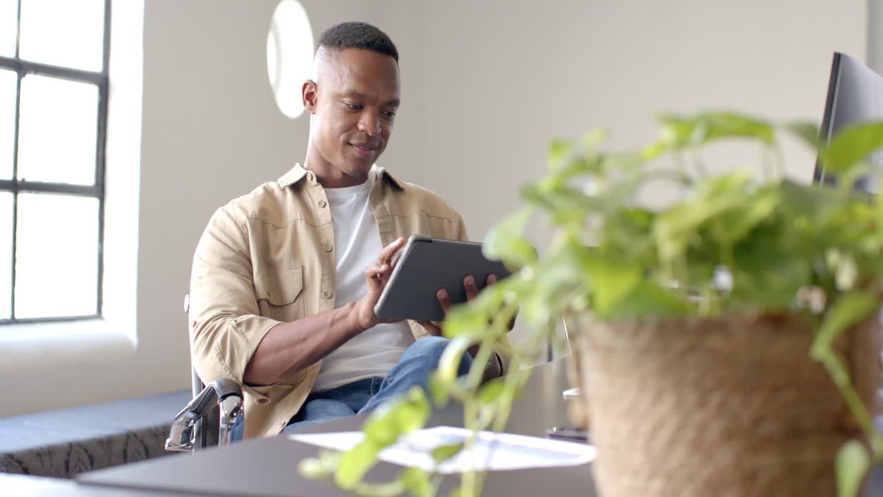 Using tablet, man sitting in wheelchair working in modern office environment