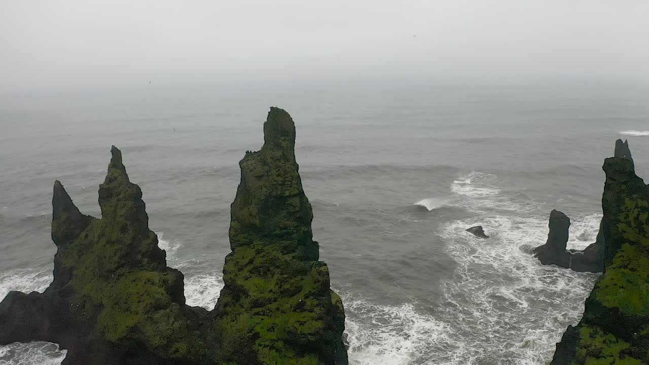 Epic moving drone shot of cliffs, dangerous black sand beach in Vík. Reynisfjara, mount Reynisfjall, Dyrholaey promontory, Iceland
