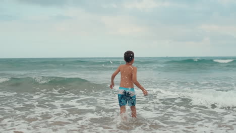 happy boy enjoying summer at beach. cheerful boy jumping in waves at seaside.