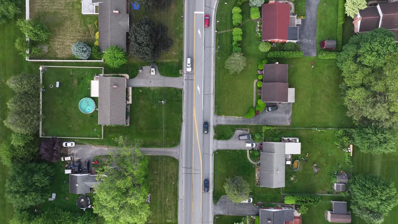 Vehicles on straight street of noble housing area in America. Spring day with green trees in quiet suburb. Aerial top down flyover shot. Pa, USA.